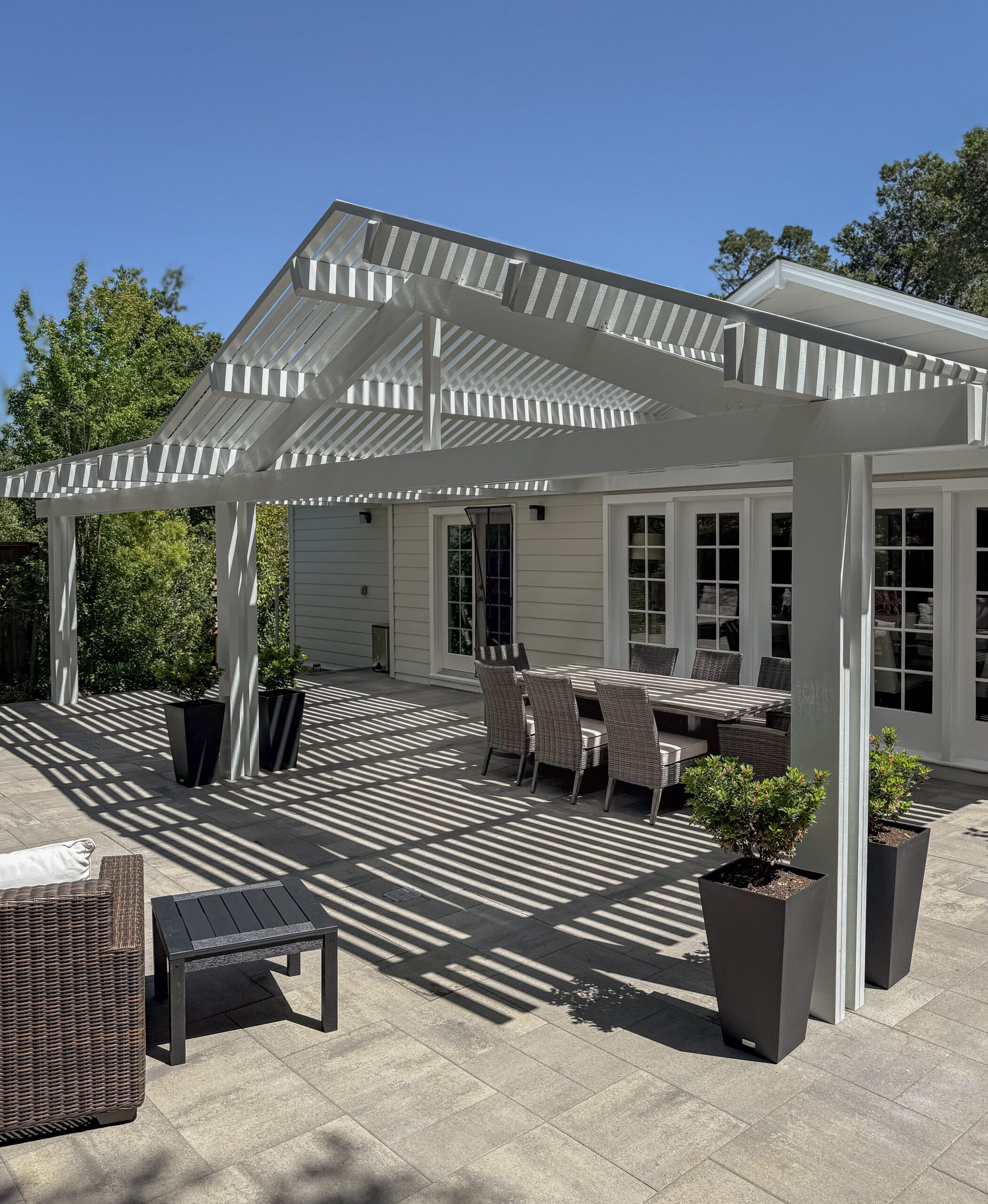 Custom white pergola over a paver patio and outdoor dining area